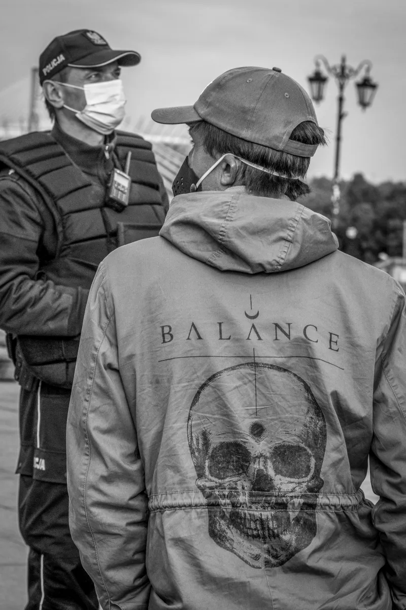 Masked man in a jacket with a skull print facing a police officer